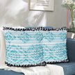 Rectangular boho pillow with aqua blue and white textured woven design and black fringe edges, styled on a modern blue couch with white throw blanket in cozy living room.