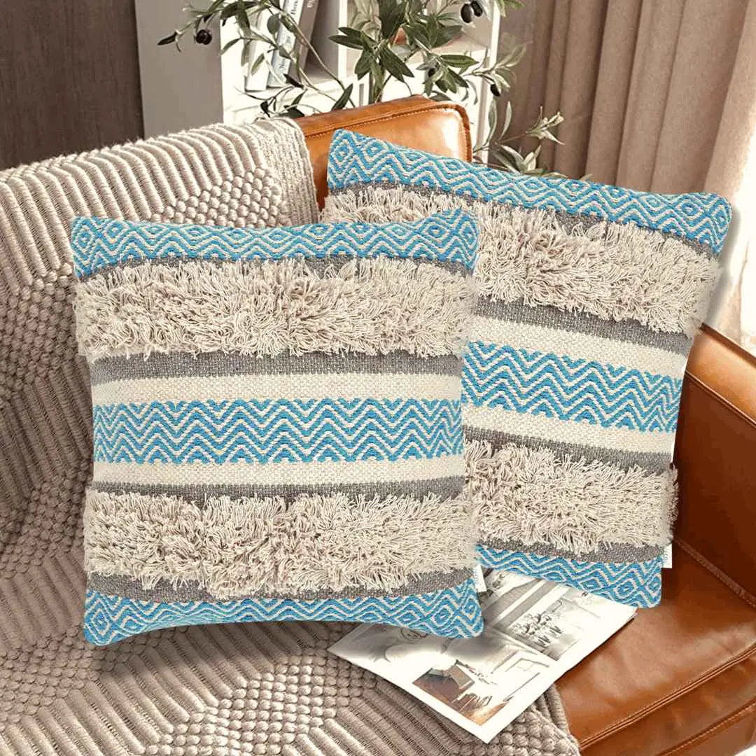 Set of two boho throw pillow covers with blue chevron patterns, beige shaggy textured stripes, and neutral gray bands, styled on a leather couch in a cozy modern living room.