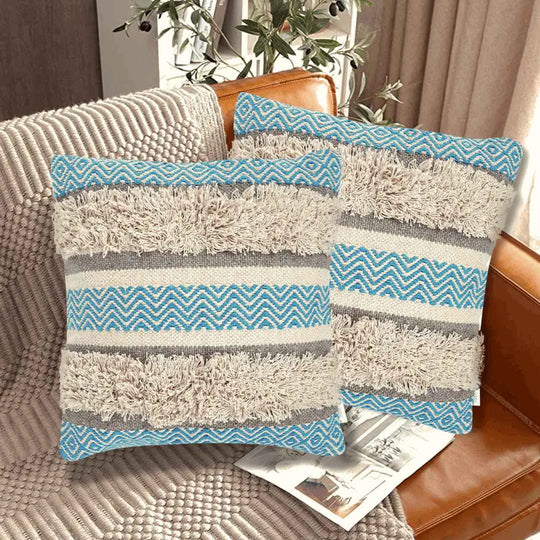 Set of two boho throw pillow covers with blue chevron patterns, beige shaggy textured stripes, and neutral gray bands, styled on a leather couch in a cozy modern living room.