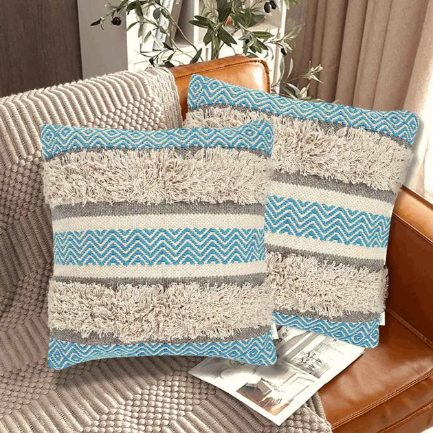 Set of two boho throw pillow covers with blue chevron patterns, beige shaggy textured stripes, and neutral gray bands, styled on a leather couch in a cozy modern living room.