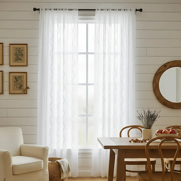 Living room with white curtains, beige armchair, wooden table, and round mirror.