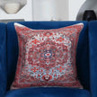"Decorative red and blue medallion throw pillow on a plush royal blue armchair, featuring a vintage Persian-inspired pattern and textured fabric design."