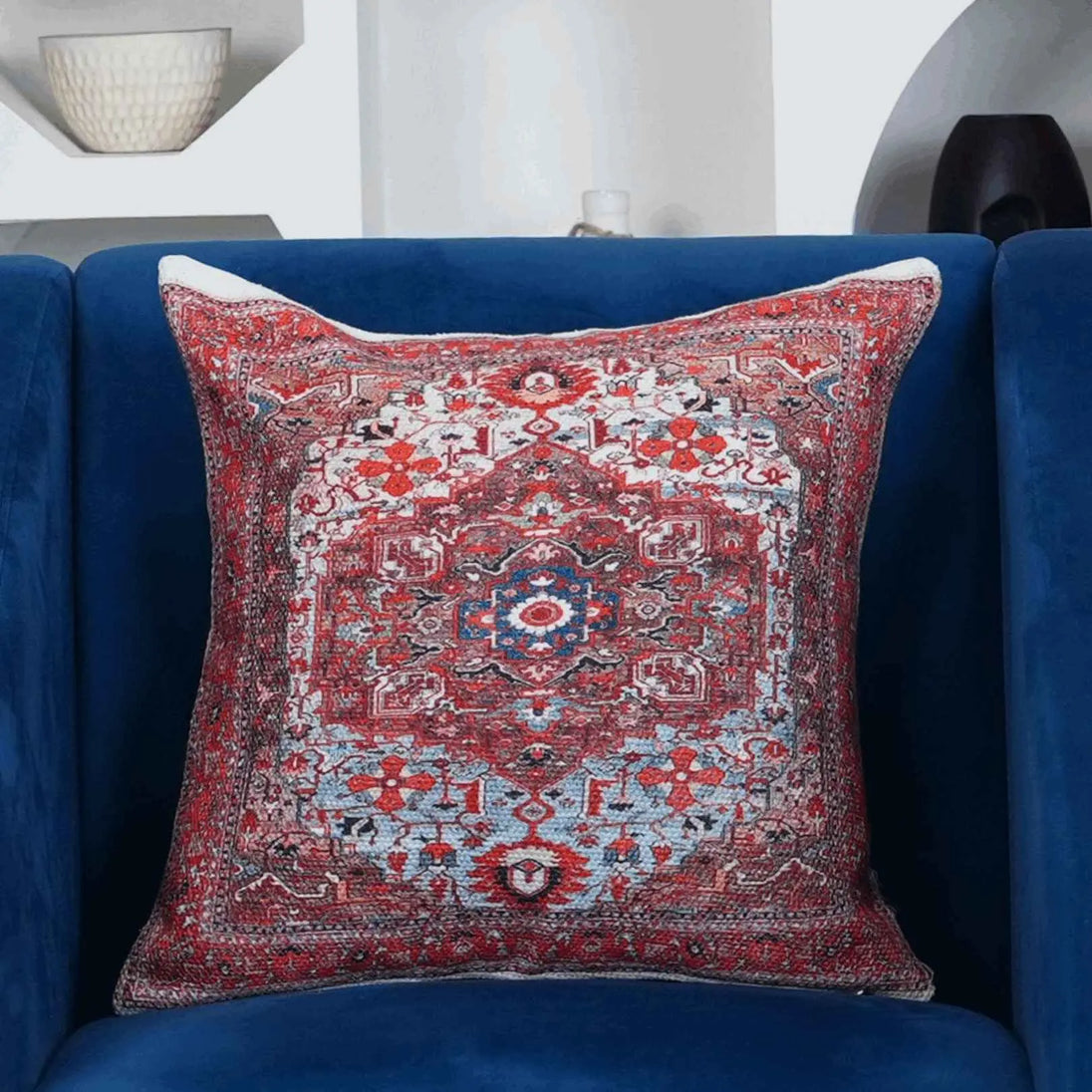 "Decorative red and blue medallion throw pillow on a plush royal blue armchair, featuring a vintage Persian-inspired pattern and textured fabric design."