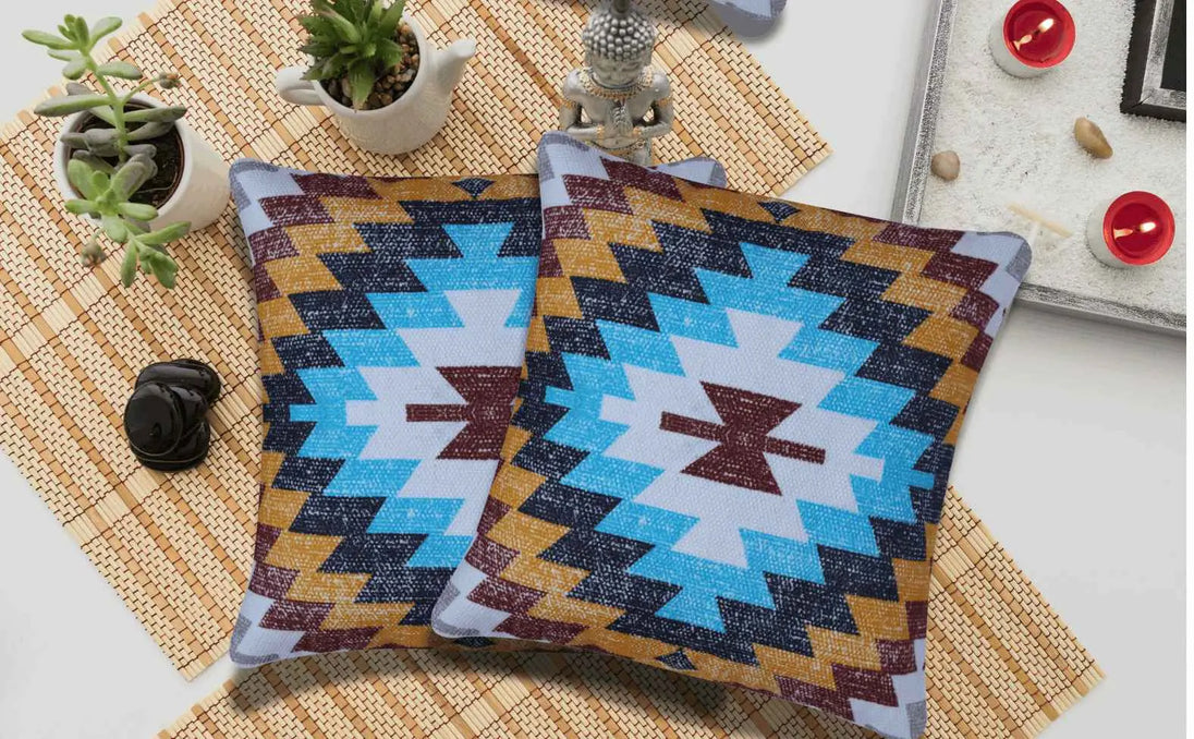 Set of two Southwestern tribal print throw pillows with bold geometric patterns in turquoise, mustard, maroon, and black, styled on a bamboo placemat with potted succulents, candles, and decorative accents for a cozy, boho vibe.