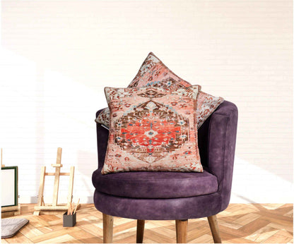 Two decorative boho-style throw pillows with red and brown medallion patterns placed on a modern purple velvet chair in a bright, minimalistic room with wooden flooring and artistic decor.