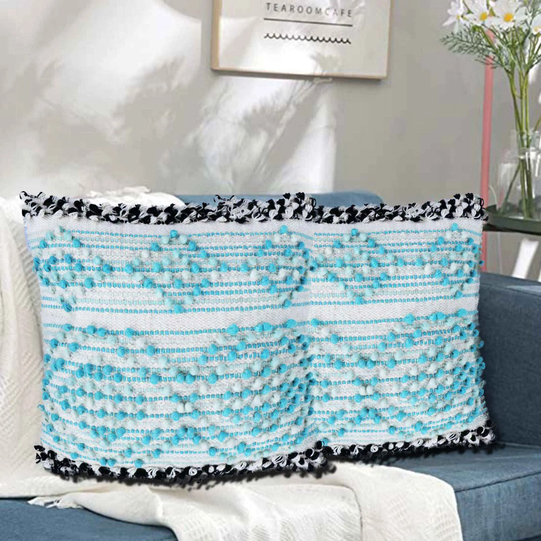 Rectangular boho pillow with aqua blue and white textured woven design and black fringe edges, styled on a modern blue couch with white throw blanket in cozy living room.