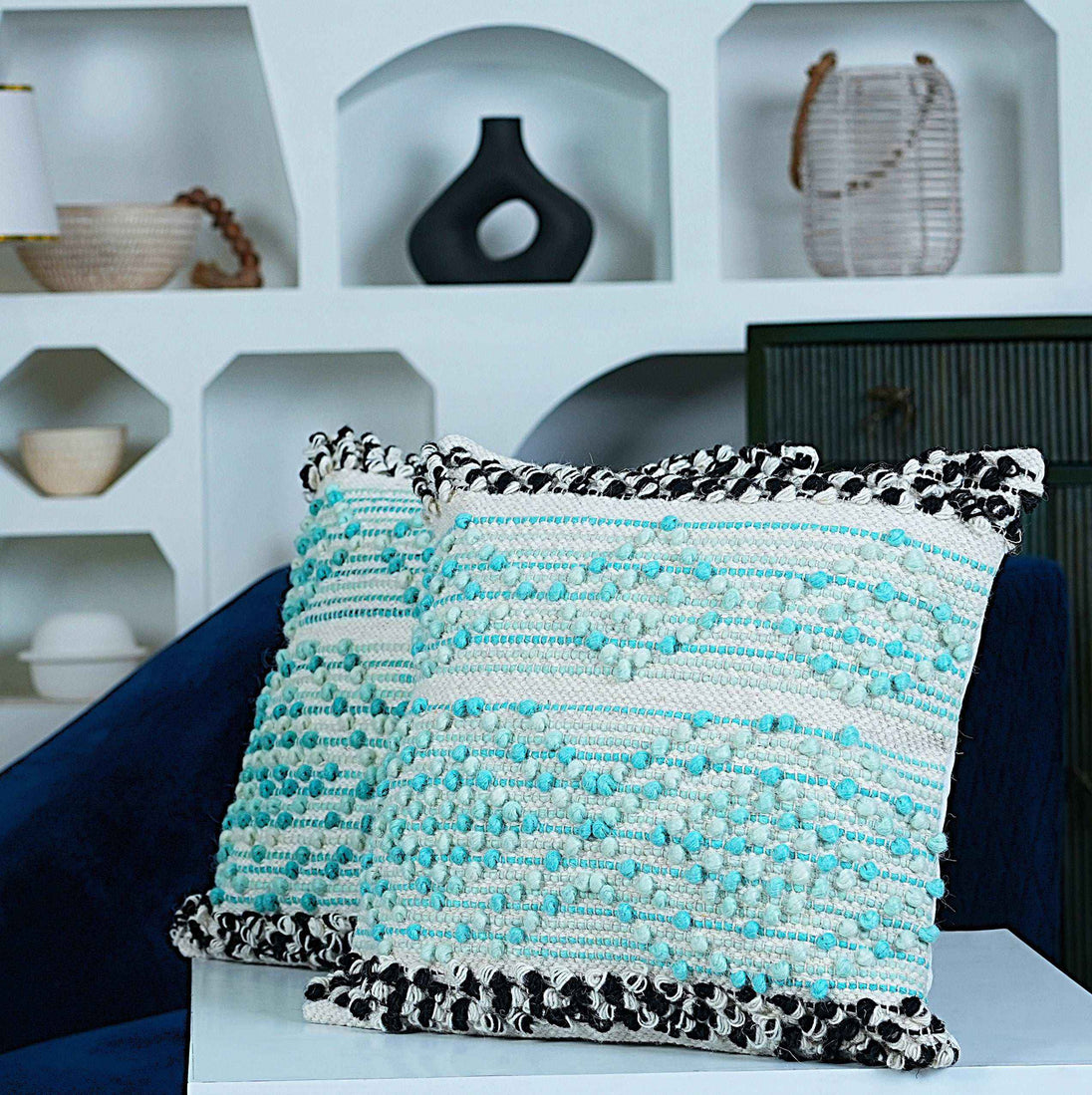 Textured aqua blue and white boho throw pillows with black woven edges on modern living room sofa, home decor accessories in background