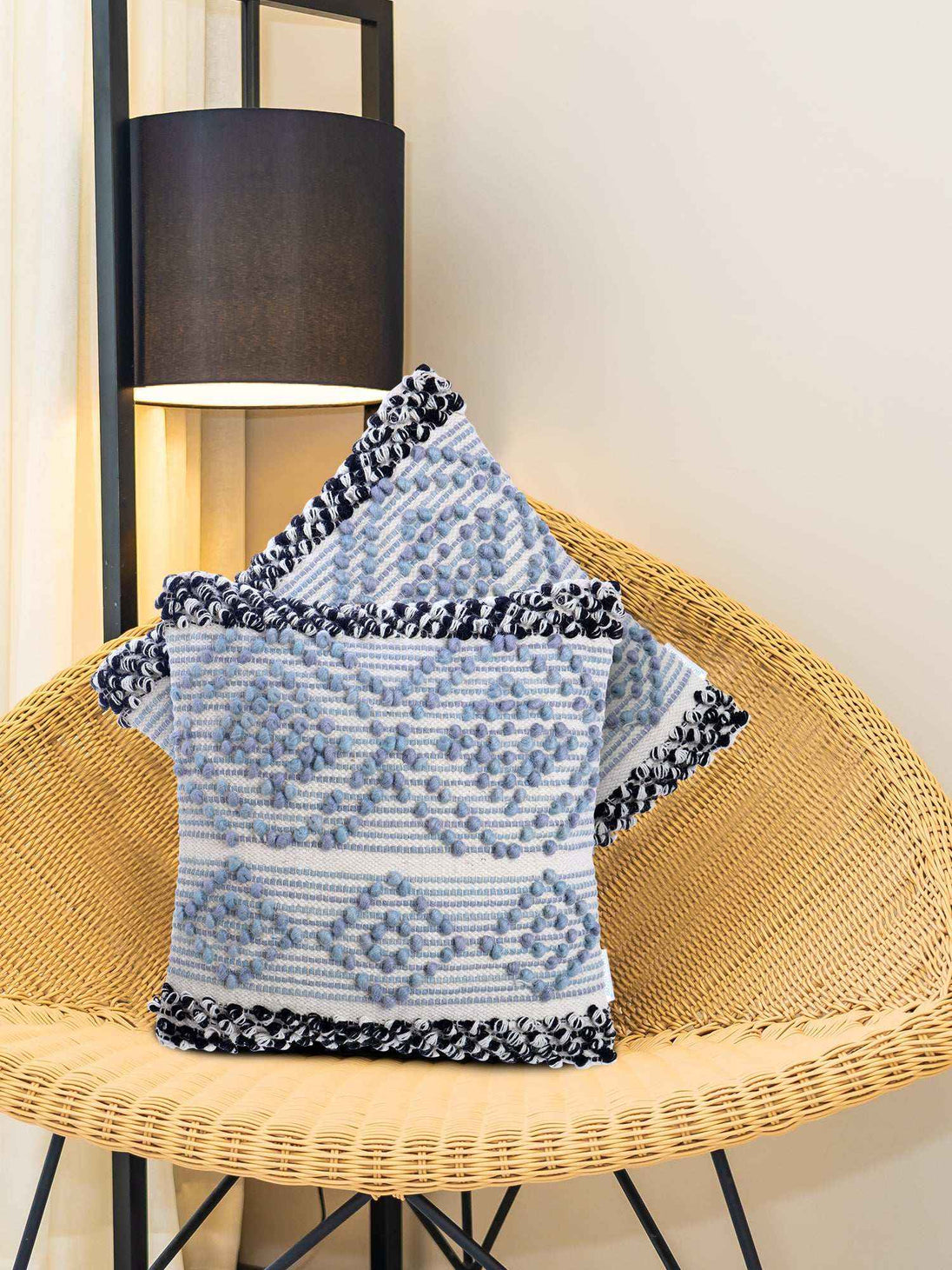 Blue tufted pillows with pom trim on rattan chair.
