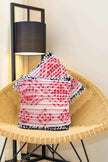 Textured red boho throw pillows on wicker chair.
