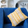 Yellow boho tufted pillow on royal blue couch.
