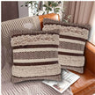 Two brown and beige decorative throw pillows with zigzag woven tufted patterns and fringe detailing, styled on a tan leather sofa with a textured throw blanket and a magazine.
