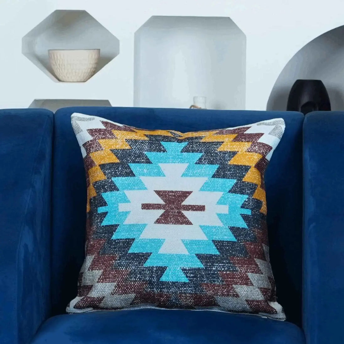 Boho Aztec decorative throw pillow cover with vibrant turquoise, mustard, and burgundy zigzag pattern — accent cushion on navy blue velvet couch for modern living room styling.