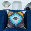 Boho Aztec decorative throw pillow cover with vibrant turquoise, mustard, and burgundy zigzag pattern — accent cushion on navy blue velvet couch for modern living room styling.