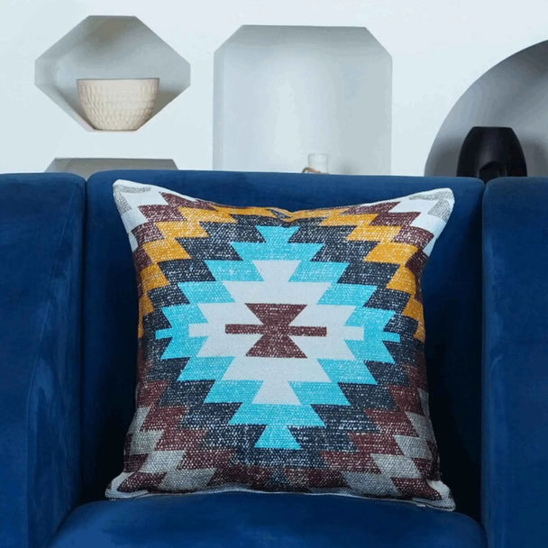 Boho Aztec decorative throw pillow cover with vibrant turquoise, mustard, and burgundy zigzag pattern — accent cushion on navy blue velvet couch for modern living room styling.