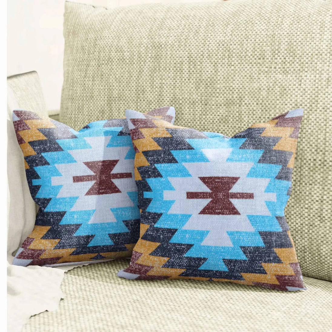 Pair of tribal print throw pillows with bold zigzag patterns in turquoise blue, mustard yellow, and maroon, placed on a textured beige sofa for a modern Southwestern home decor look.