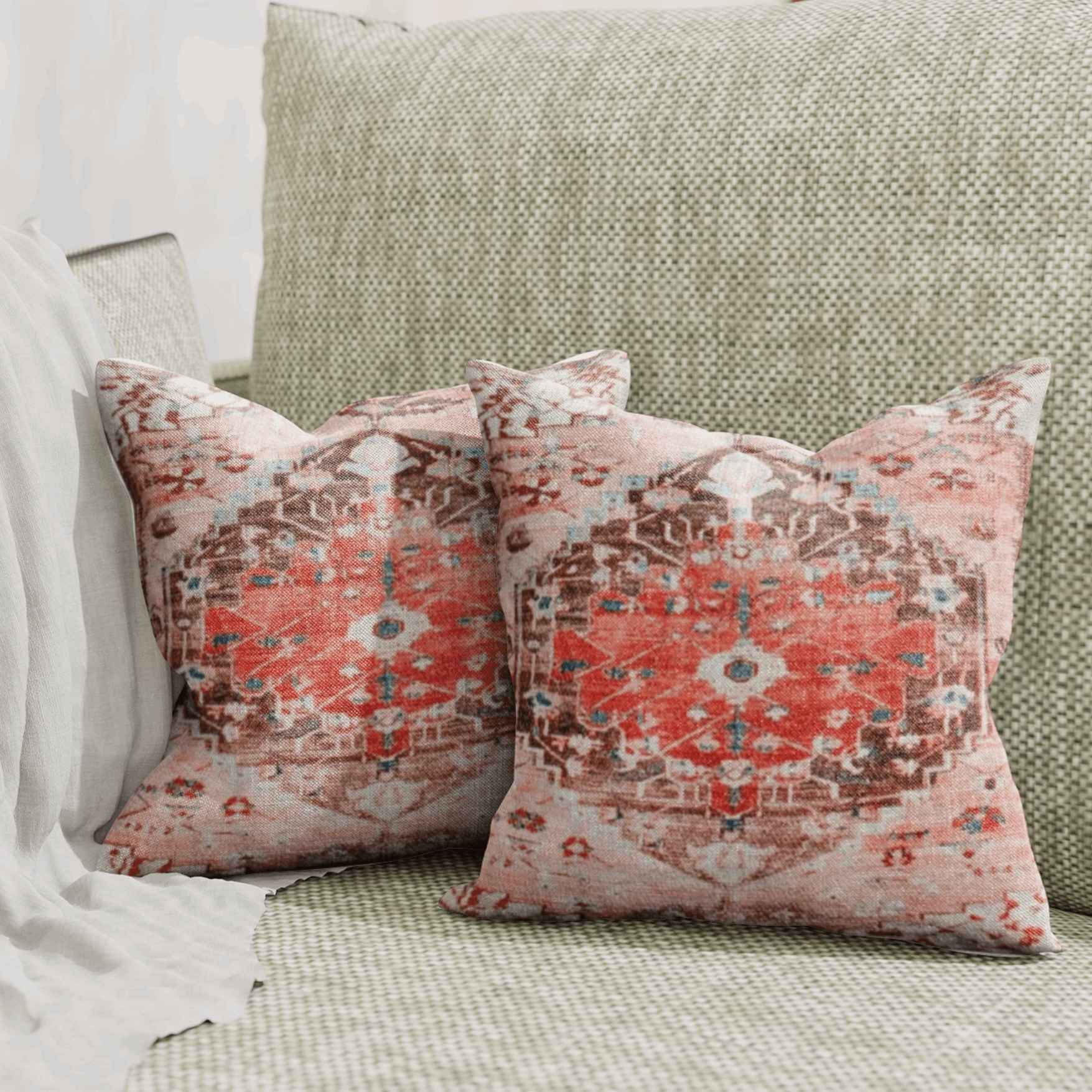 Pair of decorative throw pillows with faded red and brown circular medallion patterns resting on a textured beige sofa with a light gray throw blanket.