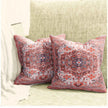 Two decorative red and blue Persian-style throw pillows placed on a textured beige sofa with a light blanket draped over the armrest.