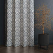 Gray damask curtain beside decorative potted tree.

